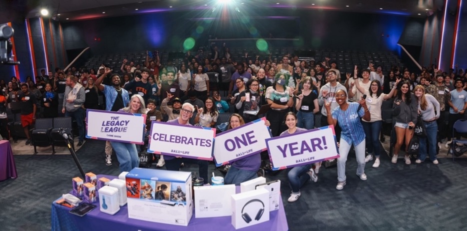 Students gather and smile for the camera with signs that say "The Legacy League celebrates one year!"