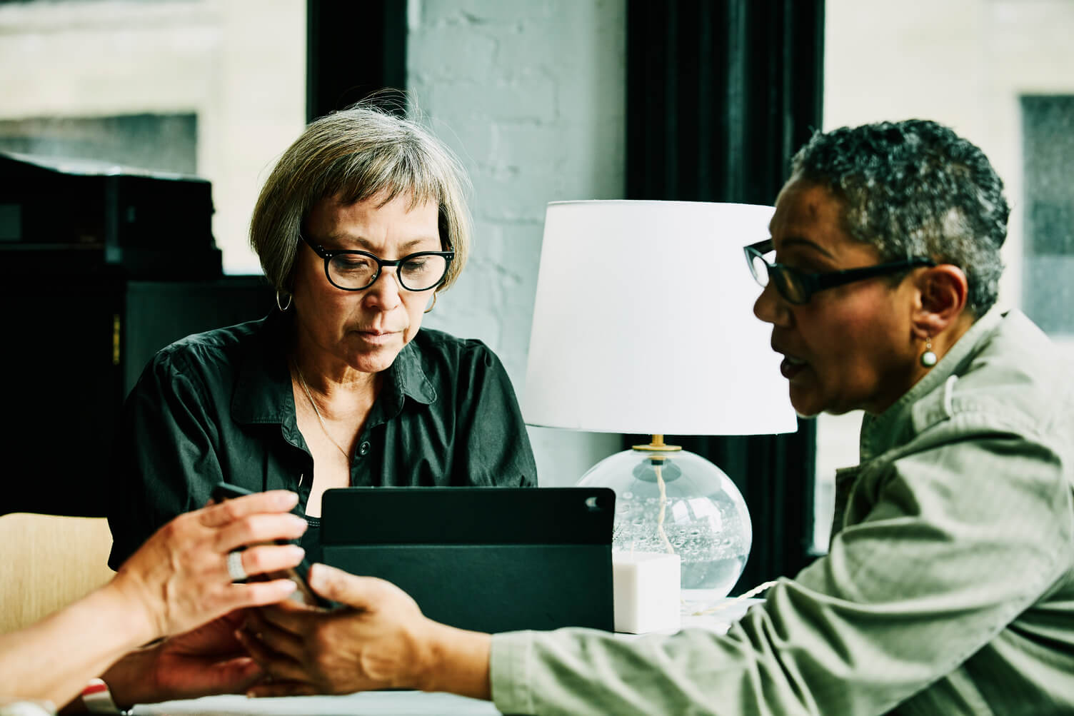 Man and woman in business attire review documents and a laptop at a desk in a bright office, supporting employment or income verification discussion.