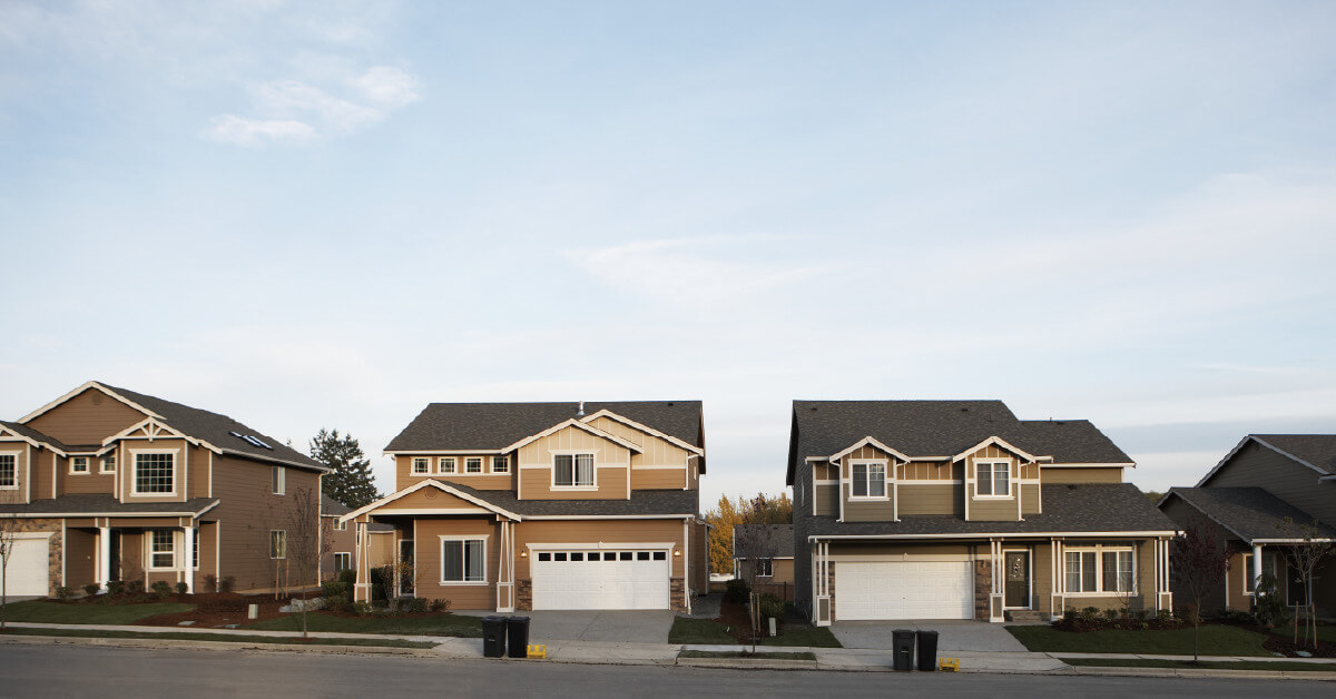 Row of modern suburban houses with attached garages along a quiet street under a clear sky.